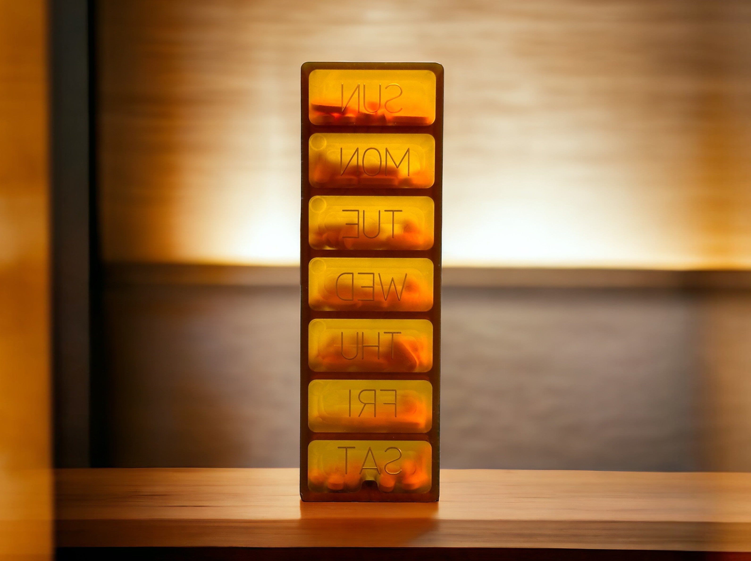 CountyComm Ultem Med Weekly PillSafe, a durable amber-colored pill organizer with seven compartments labeled for each day of the week.